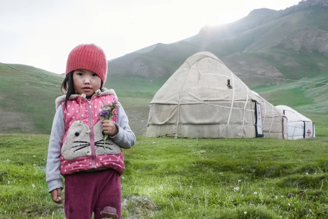 A little Kyrgyz girl with a wildflower on the background of a yurt